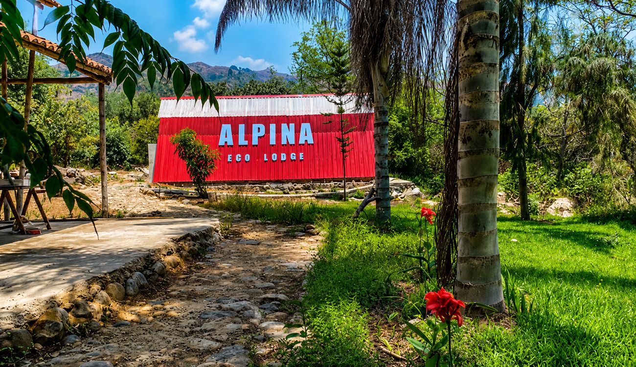 Entrada de Alpina Eco Lodge con el cartel rojo y las montañas al fondo